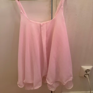 Ljusrosa ärmlös blus - Säljer en söt ljusrosa blus med dubbla lager och tunna axelband. Perfekt för sommaren nu. Blusen har en luftig passform och ett mjukt fall. Använd bara 1 gång. Storlek M men passar S väldigt bra