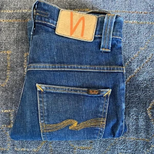 Blå jeans från Nudie Jeans - Snygga blå jeans från Nudie Jeans med klassisk lopp femficksdesign och kontrastsömmar. De har en dragkedja och knapp i gylfen samt en läderpatch med logotyp baktill. Perfekta för en stilren look.