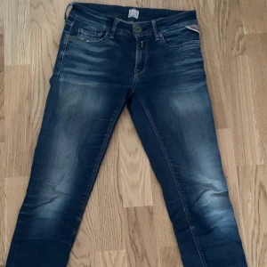 Blå jeans från Replay luz 25/30 - Snygga blå jeans från Replay med en klassisk femficksdesign och diskreta slitningar. Jeansen har en knappgylf och märkesdetaljer vid fickan och linningen. Perfekta för en avslappnad stil. Storleken är 25/30 o passar folk som är 160-165