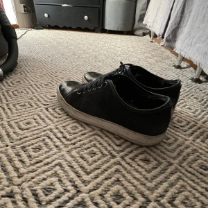 Svarta sneakers från Lanvin - Snygga svarta sneakers från Lanvin med snörning och rund tå. Perfekta för en stilren look. Sulan är vit och ger en snygg kontrast till det svarta skinnet.