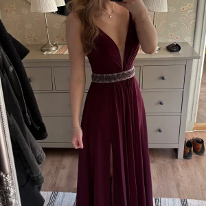 Vinröd långklänning med pärldetaljer - Elegant vinröd långklänning med djup v-ringning och smala axelband. Klänningen har en vacker pärlbroderad midja och en subtil slits framtill. Perfekt för till exempel studentbal. Klänningen är aldrig använd, bara prövad på. Säljer då jag hittat en klänning som passar mig bättre. Nypris ca 3900💞Hör gärna av dig vid frågor!