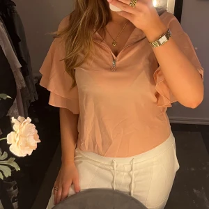 Rosa blus med volangärmar - Snygg beige blus med volangärmar och dragkedja framtill. Jättefin och vacker! Perfekt till sommaren❤️Passar M och S storleksmässigt. 