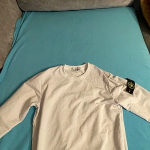 Vit t-shirt från Stone Island - Säljer en stilren vit t-shirt från Stone Island med deras ikoniska märke på ärmen. T-shirten har en klassisk rund hals och är kortärmad. Perfekt för en avslappnad och trendig look.