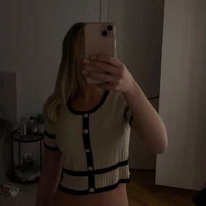 Beige  topp med knappar - Säljer en beige topp med svarta detaljer och knappar. Toppen är kortärmad och croppad. Passar bra till både jeans och kjol.💗💗