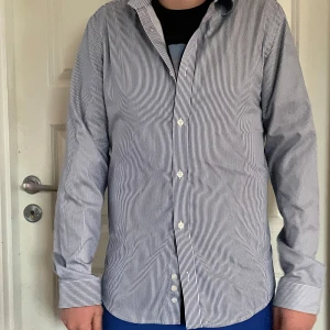 Randig skjorta från Tiger of Sweden - Snygg randig skjorta från Tiger of Sweden i blått och vitt. Skjortan har långa ärmar och knappar framtill. Perfekt för en stilren look.