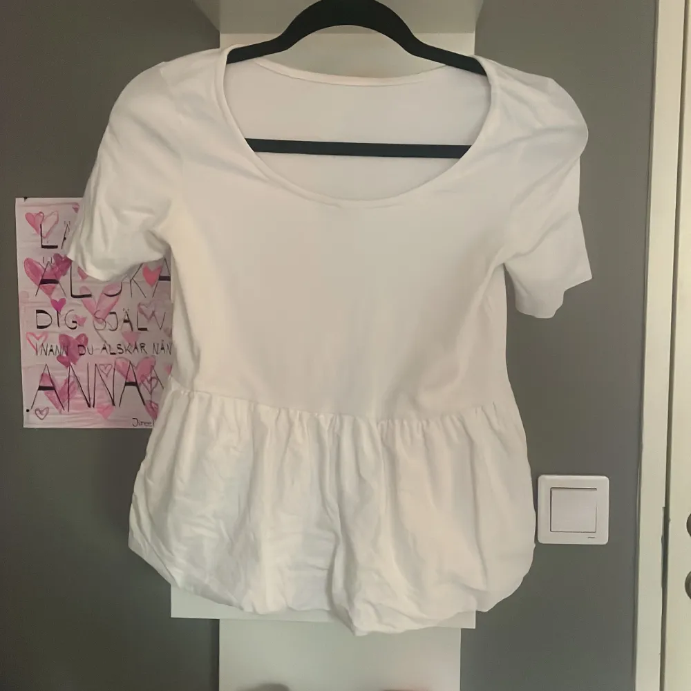 Säljer en söt vit blus med korta ärmar och volangdetalj i nederkant. Perfekt för en somrig look. Blusen har en rund halsringning och är gjord i ett mjukt material.. Yläosat.