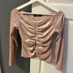 Beige/rosa sammetstopp från Bik Bok - Säljer en elegant beige sammetstopp från Bik Bok med rynkdetaljer framtill. Toppen har långa ärmar och en mjuk, glansig finish som ger en lyxig känsla.