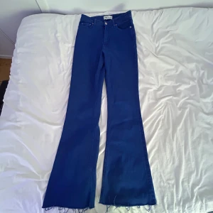 Blå bootcut jeans från Zara - Snygga blå bootcut jeans från Zara med hög midja och råa, fransiga benslut. Klassisk femficksmodell i stretchig bomullsdenim som sitter tajt upptill och släpper ut i benen. Perfekta för dig som gillar retrovibbar och vill sticka ut lite extra.