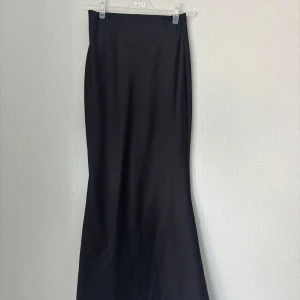 Svart sidenkjol från Boohoo - Säljer en svart långkjol från Boohoo med stilren och slät design. Kjolen har en rak och något utsvängd form som ger en snygg siluett. 