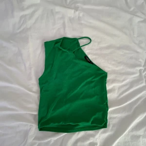 Grön oneshoulder topp från Stradivarius - Snygg grön topp från Stradivarius med asymmetrisk design och en smal axelrem. Oneshoulder-modell som ger en cool och trendig look. Tillverkad i mjukt och stretchigt material som sitter skönt på kroppen.