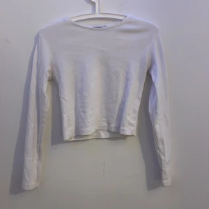 Vit långärmad topp från Stradivarius - En stilren vit långärmad topp från Stradivarius i mjuk bomull. Modellen är croppad med rund halsringning och har en enkel, clean look som passar till allt. Perfekt att matcha med jeans eller kjol för en fräsch vardagsstil. Pris kan diskuteras. 