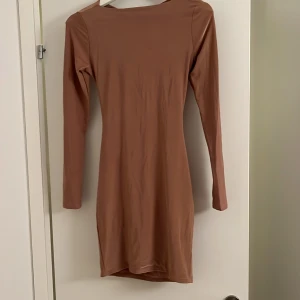 Brun omlottklänning med öppen rygg - Säljer en snygg brun kortklänning med lång ärm och cool omlott-design i ryggen. Klänningen har draperade detaljer och en öppen rygg som ger en unik look. Materialet är mjukt och stretchigt, perfekt för dig som gillar trendiga och stilrena plagg.