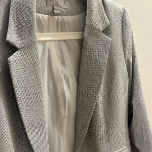 Grå mönstrad kavaj med klassisk krage - Snygg grå kavaj med diskret fiskbensmönster och klassisk krage. Kavajen har en stilren passform och är helfodrad med ljus insida. Perfekt för dig som gillar en clean och tidlös look.