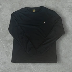 Svart långärmad tröja Polo Ralph Lauren - Svart långärmad tröja från Polo Ralph Lauren med klassisk rund hals och broderad logga på bröstet. Tröjan är i bomull och har ribbade muddar vid ärmsluten. Perfekt basic med snygg passform. OBS ‼️Det ända är att Tvätt lappen är borta. Annars ny 
