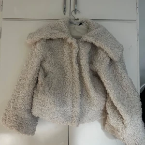 Beige teddyjacka från Divided M - Supermysig beige teddyjacka från Divided i storlek M. Jackan har en oversized krage, fluffigt teddy-material och är helfodrad. Perfekt för kalla dagar när du vill vara både varm och snygg. Passar dig som gillar en chill och trendig look.
