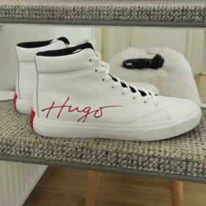Vita high-top sneakers från Hugo - Endast använda ett två gånger. Nypris: 1300. Snygga vita high-top sneakers från Hugo med röd logga på sidan och röd detalj på hälen. 