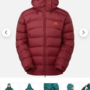 Burgundy dunjacka Mountain Equipment - Snygg vinröd dunjacka från Mountain Equipment med huva och dragkedja hela vägen. Jackan är quiltad och har en clean look utan synliga loggor förutom på bröstet. Perfekt för kalla dagar och riktigt skön passform.