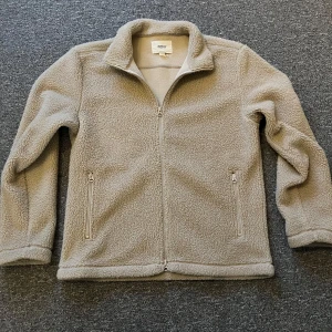 Beige teddyjacka från Dobber - Mysig beige teddyjacka från Dobber med mjuk fleeceyta och hög krage. Jackan har två fickor med dragkedja och hel dragkedja framtill. Perfekt för kalla dagar och chill stunder. Enkel, stilren design som är lätt att matcha med din garderob.