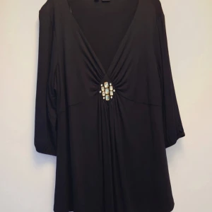 Svart tröja med smyckesdetalj Bodyflirt - Svart tröja från Bodyflirt i storlek L med djup v-ringning och snygg smyckesdetalj framtill. Klänningen har trekvartsärm och ett mjukt, följsamt tyg som ger ett elegant fall. Perfekt för dig som gillar stilrena plagg med en twist.