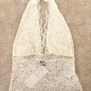 Vit spetsig halterneck topp - Supersöt halterneck topp i vit spets med blommigt mönster. Ej använd, prislapp finns kvar men säljer eftersom den tyvärr inte kommit till användning! 💞