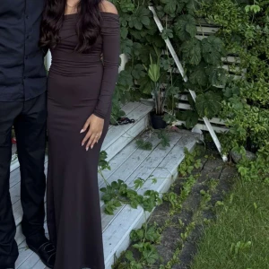 Mörkbrun offshoulder långklänning - Säljer en elegant mörkbrun långklänning med offshoulder och långa ärmar. Klänningen har figurnära passform och är tillverkad i ett stretchigt material. 