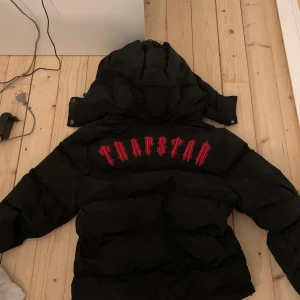 Svart pufferjacka från Trapstar - Säljer en svart pufferjacka från Trapstar med stor röd logga på ryggen den missar en knapp på luvan som syns på bilden den är äkta å har kvitto som kan visas vid intresse priset kan förhandlas vid snabb affär bara å fråga om fler bilder om de skulle velas 
