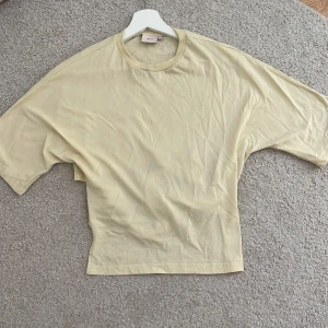 Ljus gul knyt tröja från Nelly  - Snygg ljus gul  topp från Nelly i bomull med öppen rygg och breda knytband bak. Modellen har korta ärmar och en rundad halsringning. Perfekt för dig som gillar en enkel men ändå unik look. Andvänd en gång och har en liten mörk fläck vid kragen men syns knappt ☺️