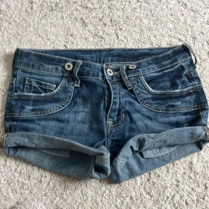 Blå jeansshorts - Snygga blå jeansshorts från Jump med klassisk femficksdesign, uppvikta benslut och dubbla knappar fram. Shortsen har kontrastsömmar och bakfickor med knappdetalj. Perfekta för varma dagar och en avslappnad stil. Köpta på secondhand i London💝💝