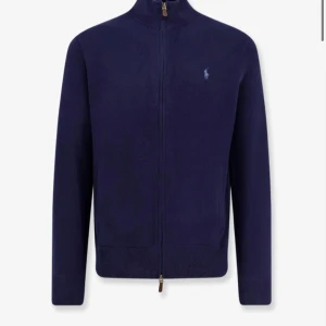 Marinblå kofta från Polo Ralph Lauren - Snygg marinblå kofta från Polo Ralph Lauren med dragkedja hela vägen och diskret broderad logga på bröstet. Tröjan är stickad och har lång ärm samt ribbade muddar. Perfekt för lager-på-lager och stilren look. Nypris ca 2500 men säljer för ca 700 eftersom den är använd. Om du bor i Stockholm möts jag gärna upp. Om ni vill ha bild på tröjan, skicka bara ett meddelande