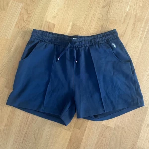 Marinblå shorts från U.S. Polo Assn. - Snygga marinblå shorts från U.S. Polo Assn. med elastisk midja och snörning. Klassisk logga broderad vid fickan och två sidofickor. Perfekta för chill dagar eller sportiga aktiviteter. Mjukt bomullsmaterial som känns skönt mot huden.