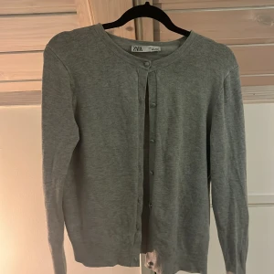 Grå kofta från Zara i bomull - Enkel och stilren grå kofta från Zara i mjuk bomull. Koftan har rund halsringning, långa ärmar och knäppning framtill med små knappar. Perfekt att slänga över en topp för en chill look.