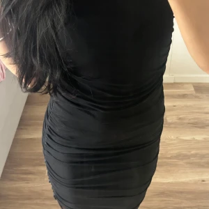 Svart tight kortklänning från NA-KD - Säljer en svart, figurnära kortklänning med snygga rynkade detaljer längs sidorna. Använd 1 gång 