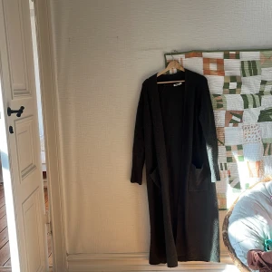 Grön lång kofta från Indiska - Säljer en grön, lång och mysig kofta från Indiska i storlek S. Koftan har två stora fickor framtill, lång ärm och är gjord i ett stickat material som känns riktigt skönt. Perfekt att slänga på sig när det är kyligt ute.