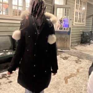Svart moose knuckles jacka med vit pälsluva  - En fin moose knuckles jacka med pälsbollar och fin luva, jackan är i storlek S men passar även xs. Använd 1 vinter och är i väldigt fint skick