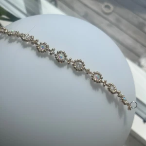 Glittrigt guldarmband med stenar - Superfint armband i guldton med runda, glittrande stenar som reflekterar regnbågens färger. Stenarna är infattade i små guldfärgade pärlor som ger ett lyxigt och festligt intryck. Perfekt accessoar för att lyfta din outfit med extra bling.