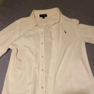 Vit skjorta från Polo Ralph Lauren - Klassisk vit skjorta från Polo Ralph Lauren med lång ärm och knappar framtill. Skjortan har den ikoniska broderade loggan på bröstet och en snygg krage. Perfekt för dig som gillar stilrena och tidlösa plagg. Skjortan är mer som slimfit 