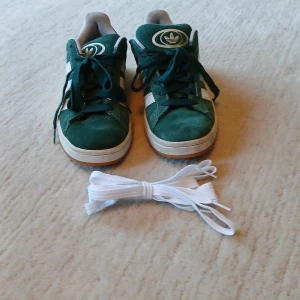 Adidas Campus gröna sneakers stl 38⅔ - Gröna Adidas Campus sneakers i mocka med vita detaljer och klassiska tre ränder på sidorna. Skorna har rund tå, platt sula och snörning. Medföljer extra vita skosnören. Perfekta för dig som gillar retrostil och streetwear. (Pris kan diskuteras)