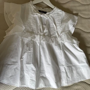 Vit volangblus från Gina Tricot XS - Supersöt vit blus i poplin från Gina Tricot med volangdetaljer på ärmar och runt bröstet.                    DEN ÄR HELT NY!!