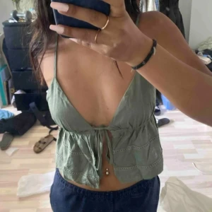 Olivgrön linnetopp - Snygg olivgrön linnetopp med smala axelband och knytband framtill. Toppen har en luftig passform med dekorativa sömmar och en lätt volangdetalj nedtill. Perfekt för varma sommardagar! Lånad första bild💚💚