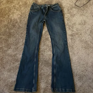 Blå jeans med broderade detaljer low waist  - Snygga blå jeans med låg midja och bootcut-stil. De har unika broderade detaljer på bakfickorna som ger en cool touch. Perfekta för dig som vill ha något annorlunda i garderoben. Strl 42 i utländsk storlek men 36/38 i svensk strl 