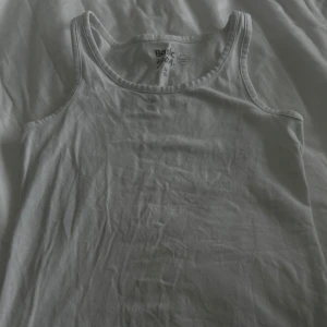 Vit linnetopp från Basic - Säljer en enkel och stilren vit linnetopp från Basic. Perfekt för varma dagar eller som lager under andra plagg. Toppen har en klassisk rund halsringning och ärmlös design.