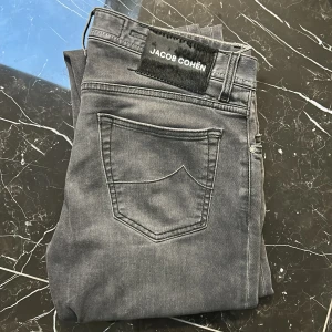 Grå jeans från Jacob Cohën - Snygga grå jeans från Jacob Cohën med klassisk femficksdesign och knappgylf. Byxorna har en stilren look med subtila detaljer och en bekväm passform.