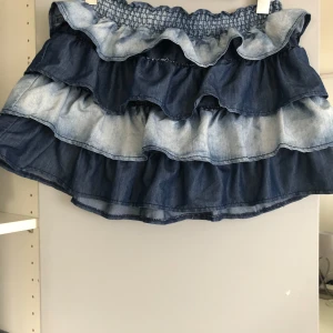 Blå volangkjol från Lindex - Säljer en söt blå volangkjol från Lindex i olika nyanser av blått. Kjolen har flera lager med volanger och en elastisk midja för en bekväm passform. Perfekt för en somrig look! 💙