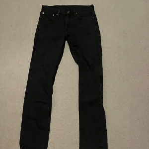 Svarta jeansbyxor från Levi's - Snygga svarta jeansbyxor från Levi's med klassisk design. De har en rak passform och är perfekta för en stilren look. Byxorna har knappar och dragkedja framtill samt fem fickor.