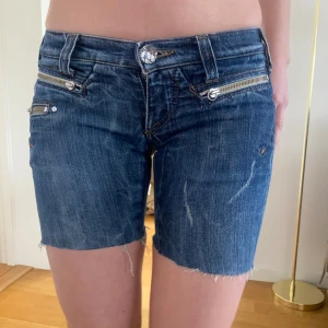 Blå jeansshorts med dragkedjor - Snygga blå jeansshorts med slitna detaljer och dragkedjor framtill. 