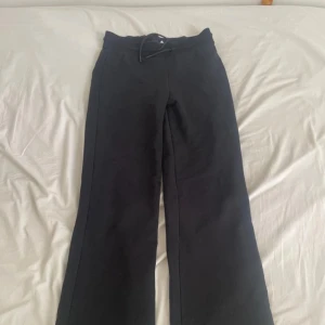 Svarta byxor med vida ben - Snygga svarta byxor med vida ben och hög midja. Perfekta för en stilren look. Byxorna har en enkel design utan mönster och är tillverkade i ett mjukt material.