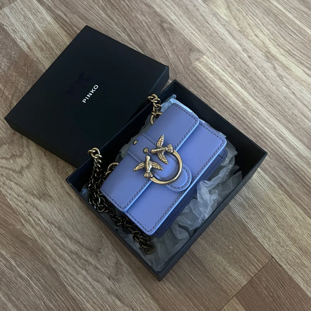 Säljer en helt ny snygg ljuslila axelväska från Pinko med guldfärgade detaljer och kedja. Väskan har ett dekorativt spänne med fåglar framtill och är perfekt för att ge din outfit en färgklick. Kommer i originalförpackning.. Laukut & Käsilaukut.