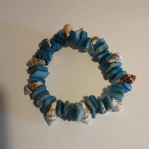 Blått armband med snäckor - Unikt armband med blå detaljer och små snäckor. Perfekt för en strandlook eller sommarens äventyr. Elastiskt band för enkel passform. Armbandet är cirka 6 cm i diameter samt 16 cm i omkretsen.