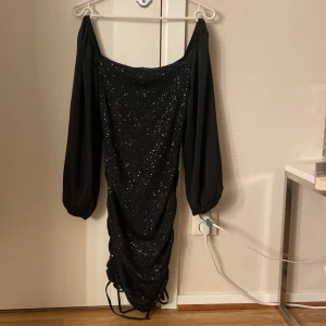 Svart glittrig klänning - Svart glittrig kläning som kan användas som offshoulder, men även som långärmad, snören vid sidorna som man kan justera, kläningen kan justeras kort-lång med hjälp av snören 💕använd 1 gång