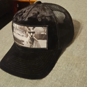 Svart keps med tryck - Snygg svart keps från Flexfit med en fet bild på en kängeru i solglasögon och en fin bil i bakgrunden. Kepsen har en böjd skärm och mesh på baksidan för bättre ventilation. Perfekt för en avslappnad stil.